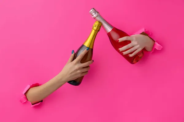 Dos manos femeninas con botella de vino blanco y rosa atraviesan el fondo de papel rosa — Foto de Stock