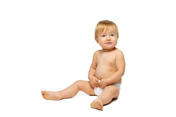 Retrato de pequeño niño lindo, bebé en pañal sentado aislado sobre fondo blanco del estudio. Ojos azules — Foto de Stock