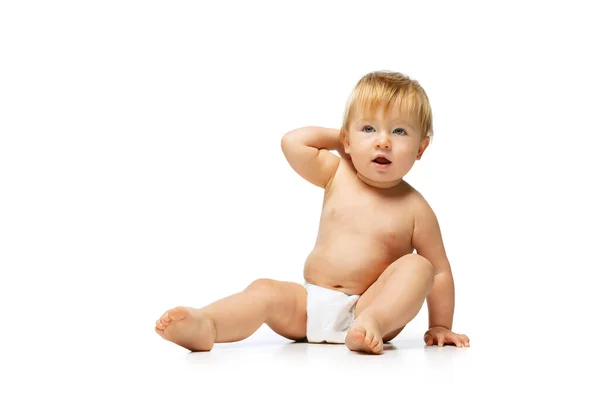 Portret van kleine schattige peuter jongen, baby in luier zit geïsoleerd over witte studio achtergrond. Nieuwsgierig, attent kind. — Stockfoto