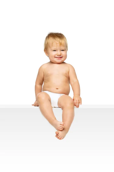 Portret van kleine schattige peuter jongen, baby in luier zitten geïsoleerd over witte studio achtergrond. — Stockfoto