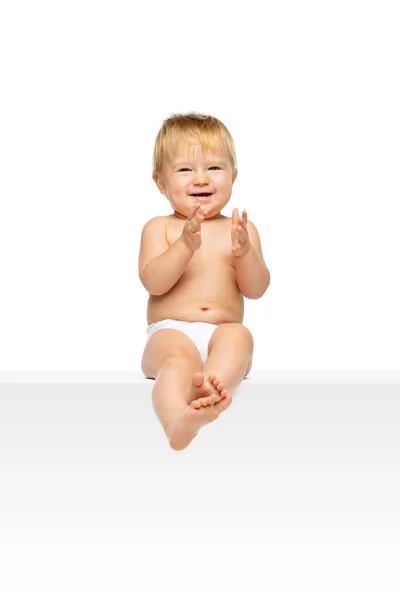 Portret van kleine schattige peuter jongen, baby in luier zit geïsoleerd over witte studio achtergrond. Klappende handen — Stockfoto