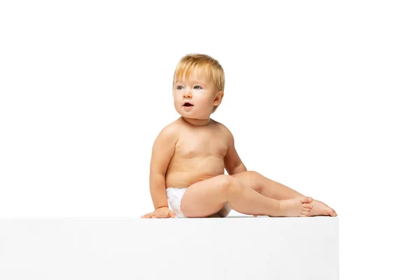 Portret małego słodkiego maluszka, dziecka w pieluszce siedzącego samotnie na białym tle studia. Widok boczny — Zdjęcie stockowe