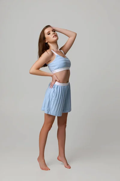 Full-length portrait of beautiful young woman in blue pajamas posing isolated over gray background — Stock Photo, Image