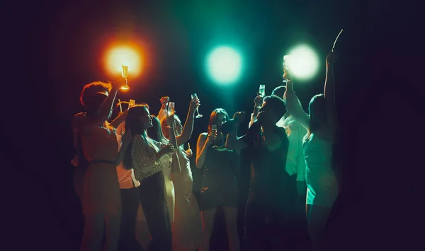 Group of young, active people at the night club, party dancing in neon lights