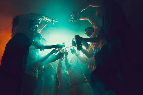 Group of young, active people at the night club, party dancing in neon lights, drinking cocktails