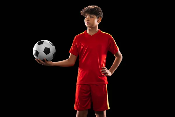 Retrato recortado de niño, adolescente, jugador de fútbol profesional en uniforme con la pelota posando aislado sobre fondo negro —  Fotos de Stock