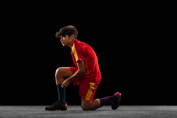 Ritratto di ragazzo, adolescente, calciatore professionista raddrizzare clothesm, calzini isolati su sfondo nero — Foto Stock