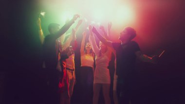 Gece kulübünde bir grup genç ve aktif insan neon ışıklarda dans ediyor.