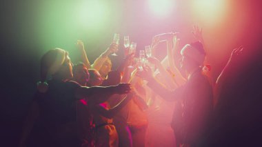 Gece kulübünde bir grup genç ve aktif insan neon ışıklarda dans ediyor. Mutlu yıllar.