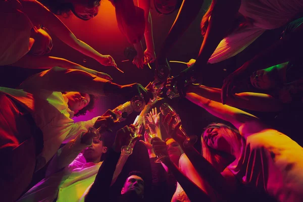 Botten utsikt över klinkande glasögon. Grupp av unga, aktiva människor på nattklubben, fest i neonljus, dricka cocktails — Stockfoto
