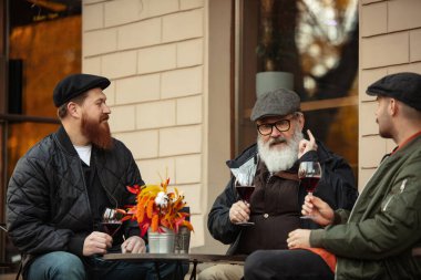 Bir grup erkek, arkadaşlar sıcak bir sonbahar gününde kafede toplanıyorlar. Kırmızı şarap içip, kadeh tokuşturuyorum.