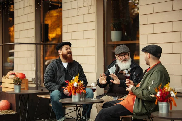 Gruppo di uomini, amici che hanno un incontro al caffè nella calda giornata autunnale. Bere vino rosso, bicchieri di clinking — Foto Stock