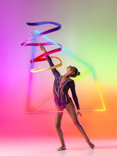 Obra creativa de gimnasta rítmica femenina profesional en movimiento con cinta brillante sobre elemento geométrico de neón aislado sobre fondo multicolor — Foto de Stock