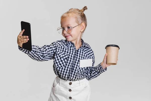 Vágott portré aranyos kislány telefon és kávéscsésze elszigetelt szürke háttér — Stock Fotó