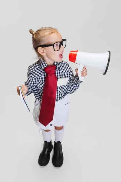 Cropped portrait of cute little girl in casual clothing shouting in megaphone isolated over gray background — Stock Photo, Image