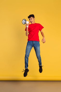 Sarı arka planda izole edilmiş megafonla kırmızı tişörtlü bir gencin tam boy portresi.