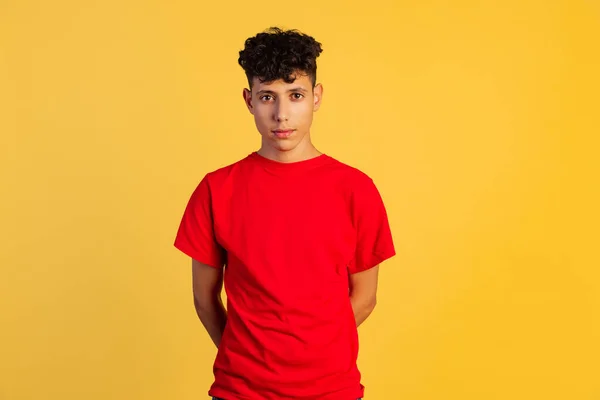 Vágott portré fiatal fiú piros pólóban nyugodtan néz kamera elszigetelt sárga háttér — Stock Fotó