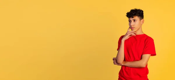 Retrato recortado de un niño joven con una camiseta roja cuidadosamente mirando hacia otro lado, aislado sobre un fondo amarillo. Volante —  Fotos de Stock