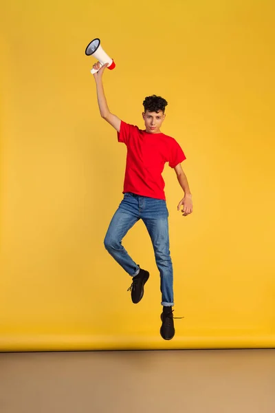 Portret młodego chłopca w czerwonej koszulce z megafonem skaczącym na żółtym tle — Zdjęcie stockowe