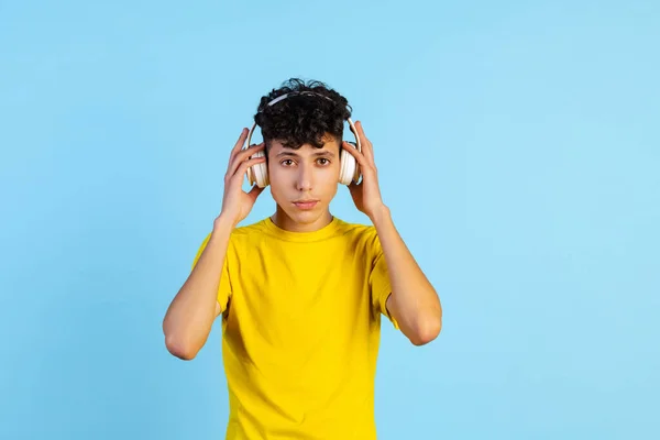 Retrato recortado de menino em camiseta amarela usando fones de ouvido isolados sobre fundo azul — Fotografia de Stock