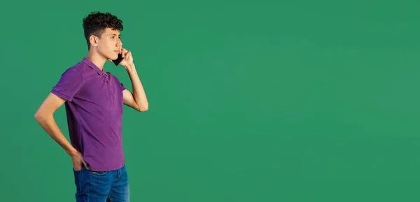 Vágott oldalnézet portré fiatal fiú lila pólóban beszél telefonon elszigetelt zöld háttérrel. Szórólap — Stock Fotó