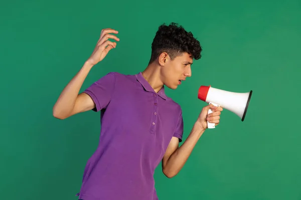 Retrato recortado de jovem rapaz de t-shirt roxa falando em megafone isolado sobre fundo verde. Partilha de informações — Fotografia de Stock