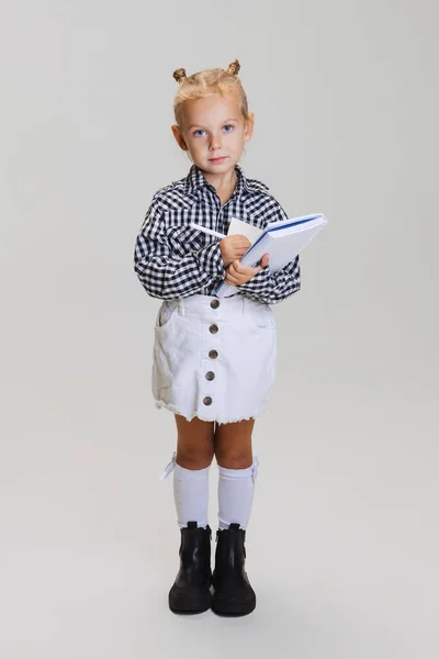 Retrato de comprimento completo de menina bonito, criança em camisa quadriculada fazendo notas isoladas sobre fundo cinza — Fotografia de Stock