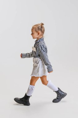 Küçük tatlı kızın tam boy yan görünüm portresi, kareli tişörtlü çocuk gri arka planda tek başına kalıyor.