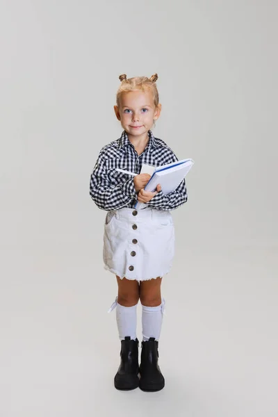 Retrato de comprimento completo de menina bonito, criança em camisa quadriculada fazendo notas isoladas sobre fundo cinza — Fotografia de Stock