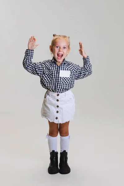 Full-length vista lateral retrato de pouco bonito menina, criança na saia e xadrez camisa posando isolado sobre fundo cinza — Fotografia de Stock