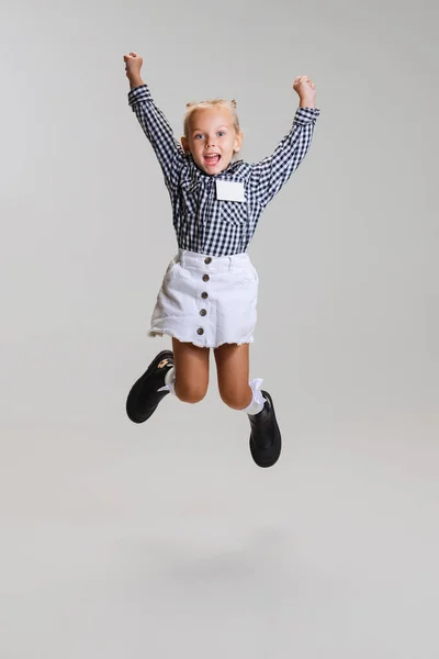 Full-comprimento vista lateral retrato de menina bonito pouco, criança na saia e camisa quadriculada pulando isolado sobre fundo cinza — Fotografia de Stock