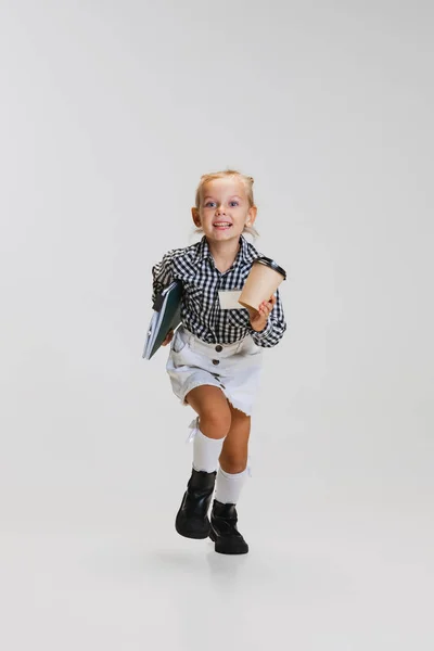 Pełna długość boczny widok portret małej uroczej dziewczyny, dziecko w spódnicy i koszuli w kratkę działa samodzielnie na szarym tle — Zdjęcie stockowe