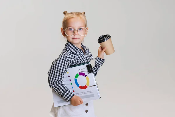 Full-length side view portrait of little cute girl, child in skirt and checkered shirt wearing stylish glasses isolated over gray background — Stock Photo, Image