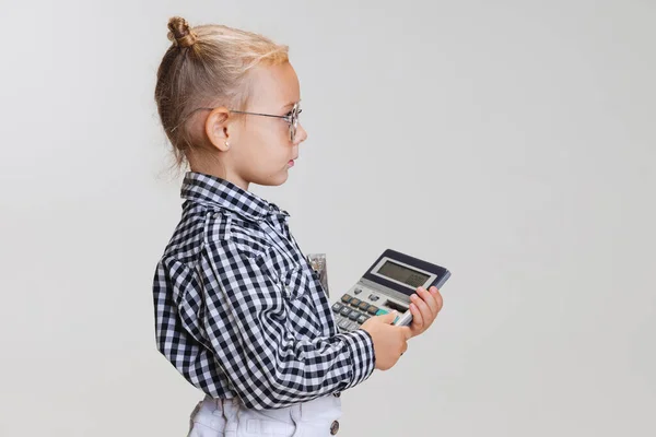 Cropped side view portrait of little cute girl, child in skirt and checkered shirt with calculator isolated over gray background — Stock Photo, Image