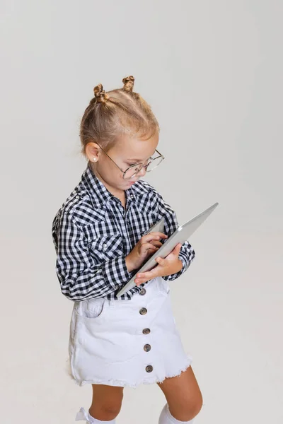 Gesneden portret van klein meisje, kind typen op tablet geïsoleerd over grijze achtergrond — Stockfoto