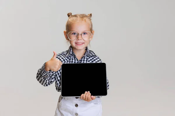 Ritratto ritagliato di carina bambina, tablet bambino in possesso isolato su sfondo grigio. Come un gesto — Foto Stock