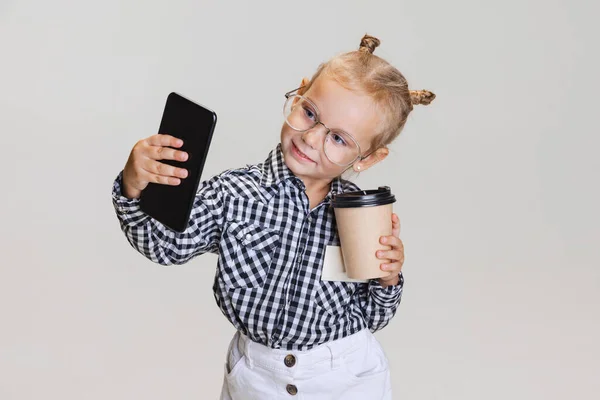 Ritratto ritagliato di carina bambina, bambino che prende selfe con telefono e tazza di caffè isolato su sfondo grigio — Foto Stock