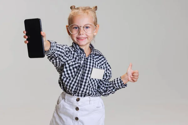 Vágott portré aranyos kislányról, gyerek mutatja telefon elszigetelt szürke háttér. Mint egy gesztus. — Stock Fotó