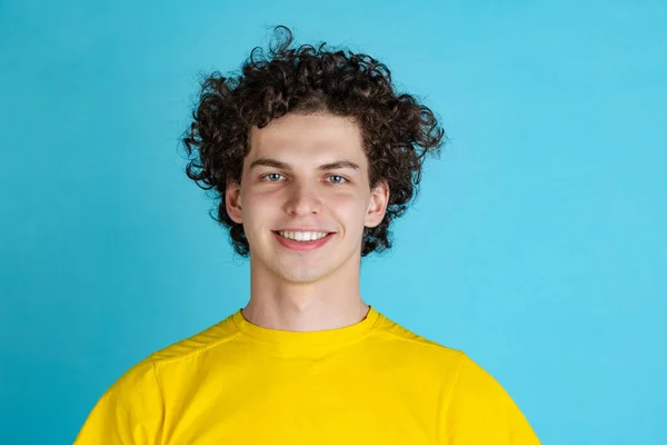 Обрезанный портрет молодого улыбающегося мужчины в желтой футболке, изолированный на синем фоне. Восхитительное выражение лица — стоковое фото