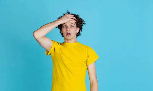 Ausgeschnittenes Porträt eines jungen Mannes in gelbem T-Shirt, der schockiert die Stirn berührt, isoliert über blauem Hintergrund — Stockfoto