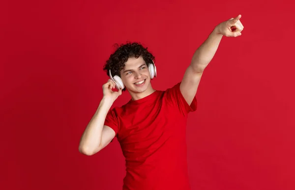 Ausgeschnittenes Porträt eines jungen Mannes in lässigem Tuch, der mit Kopfhörern fröhlich Musik hört und irgendwo isoliert auf rotem Hintergrund zeigt — Stockfoto