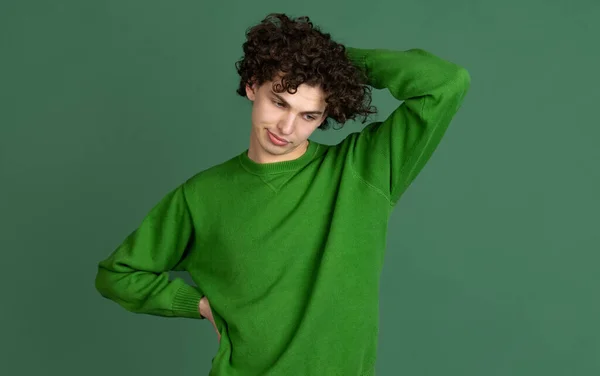 Retrato recortado de jovem em suéter verde com expressão facial de mal-entendido isolado sobre fundo verde escuro — Fotografia de Stock