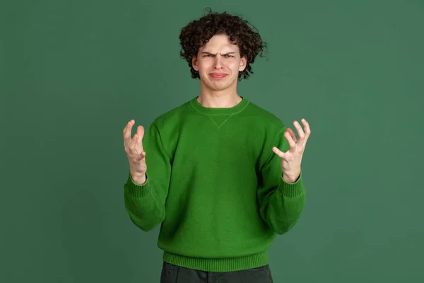緑のセーターの若い男のトリミングされた肖像画ともにイライラ顔の表現の誤解隔離された暗い緑の背景 — ストック写真