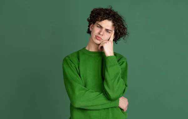 Cropped portrait of young man in green sweater with thinking facial expression isolated over dark green background — Stock Photo, Image