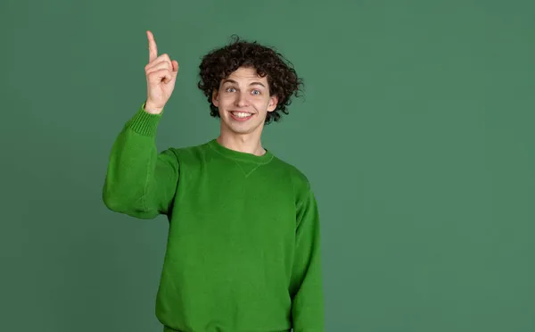 濃い緑色の背景の上に隔離された興奮した表情を持つ緑のセーターの若い男のトリミングされた肖像画。アイデア — ストック写真