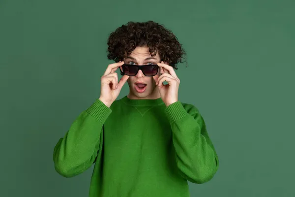 Retrato recortado de jovem em suéter verde e óculos de sol elegantes isolados sobre fundo verde escuro. Juventude na moda — Fotografia de Stock