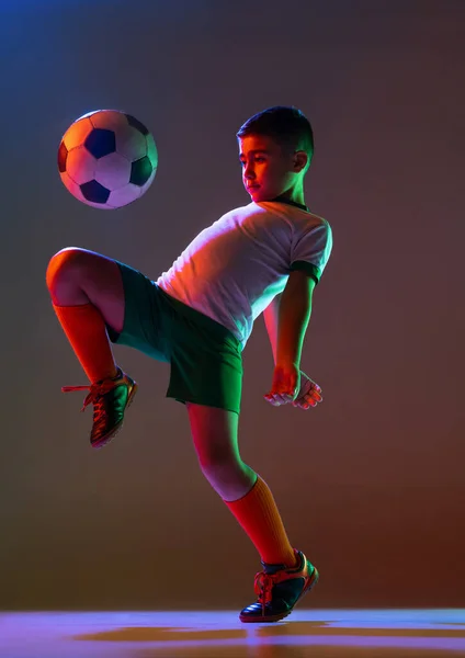 Portrait complet de garçon, jeu d'enfant, football d'entraînement isolé sur fond de gradient sous la lumière du néon — Photo