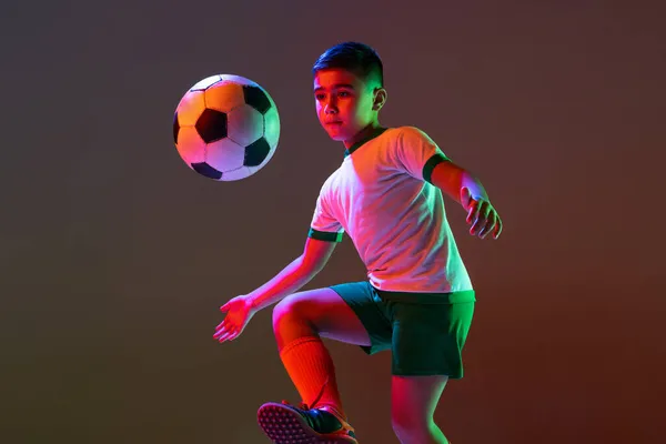 Ritratto ritagliato di ragazzo, bambino, allenamento giocatore di calcio con palla isolata su sfondo sfumato in luce al neon. — Foto Stock