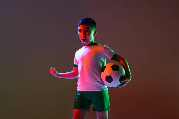 Portret chłopca, dziecka, piłkarza pozowanie na gradientowym tle w neonowym świetle — Zdjęcie stockowe