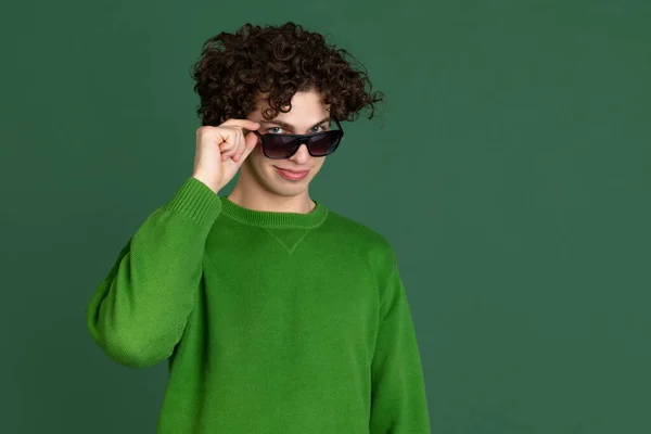 Portret młodego mężczyzny w zielonym swetrze w stylowych okularach przeciwsłonecznych odizolowany na ciemnozielonym tle — Zdjęcie stockowe